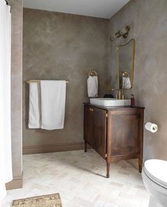 a white toilet sitting next to a wooden cabinet in a bathroom on top of a hard wood floor