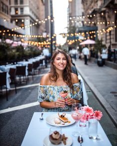 a woman sitting at a table with food and drinks in front of her on the street