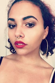 an image of a woman with piercings on her nose and wearing red lipstick in front of a white wall