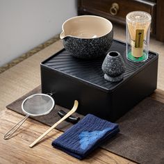 a tea tray with two cups and a strainer on it, next to a pair of bamboo utensils