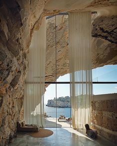 an open room with sheer curtains on the windows and stone walls, along with a dog laying on the floor