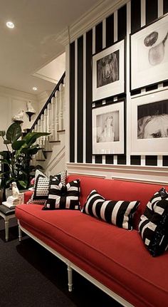 a red couch with black and white pillows is in front of some pictures on the wall