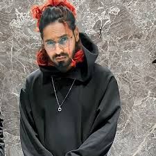 a man with red hair wearing a black hoodie and standing in front of a stone wall