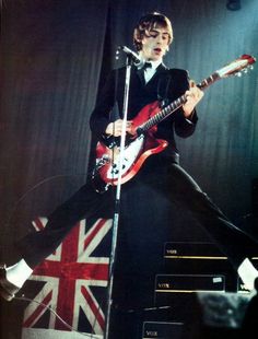 a man in a tuxedo playing an electric guitar on stage with the british flag behind him