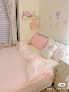 a bed with pink sheets and pillows in a small room next to a white dresser