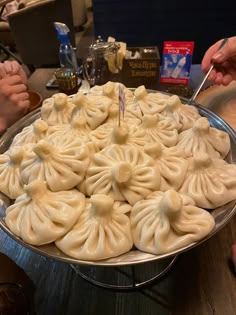 a large plate filled with dumplings sitting on top of a table next to two people