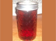 a jar filled with red liquid sitting on top of a wooden table next to a computer keyboard