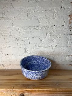 a blue and white bowl sitting on top of a wooden table next to a brick wall