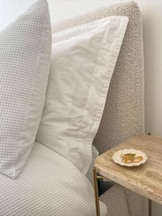 a small table with a plate on it next to a white bed and pillows in a room