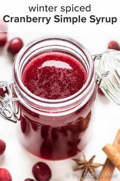 cranberry sauce in a glass jar surrounded by fresh cranberries and cinnamon sticks