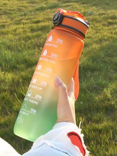 a person holding a water bottle in their left hand on the grass with an orange strap around it