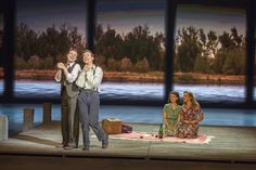 two men and a woman standing on a stage in front of a body of water