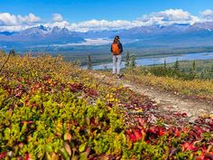 a person with a backpack walking on a trail in the mountains near water and trees