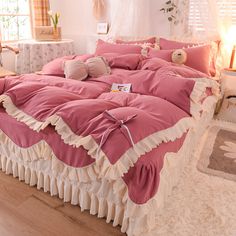 a bed with pink sheets and ruffled edges in a bedroom area next to a window