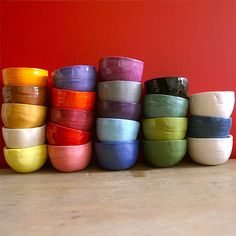 a stack of colorful bowls sitting on top of a wooden table next to a red wall