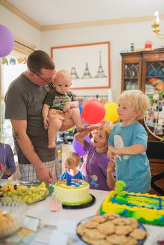 a group of people standing around a table with cakes and balloons