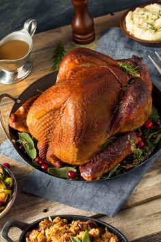 a roasted turkey in a cast iron skillet on a wooden table with other dishes and utensils