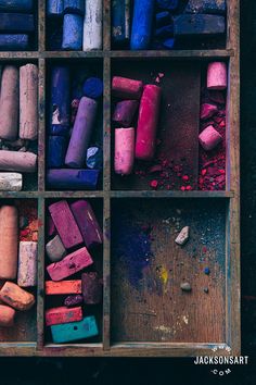 there are many different colored crayons in this wooden box with rocks and gravel