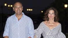 a man and woman holding hands walking down the street at night with lights in the background