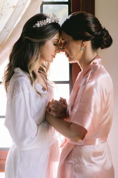 two women standing next to each other in front of a window wearing pink robes and tiaras