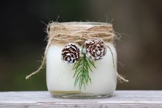 a mason jar with pine cones and twine on the top is sitting on a wooden table