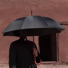 a man holding an umbrella in front of a brown building with a small window on the side