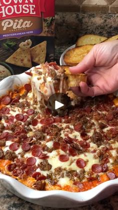 a person dipping a piece of pizza into a casserole dish with pepperoni and cheese