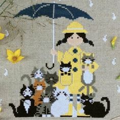 a cross stitch picture with cats and a woman holding an umbrella