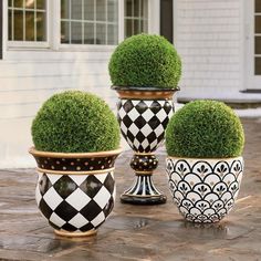 three black and white vases with green topiary balls in them on a patio