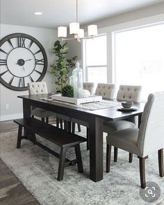 a dining room table and chairs with a clock on the wall behind it in front of a window