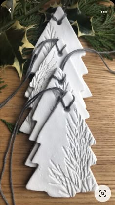 three white ceramic christmas trees are sitting on a wooden table next to evergreen leaves and twine