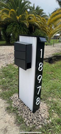 a black and white mailbox sitting on top of a grass covered field next to palm trees