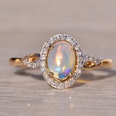 an oval opal and diamond ring on a wooden surface, with the center stone surrounded by small white diamonds