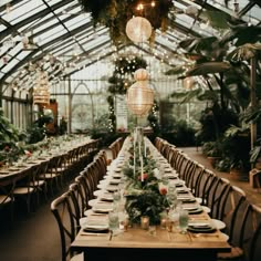 a long table set up with place settings and greenery for an event in a greenhouse