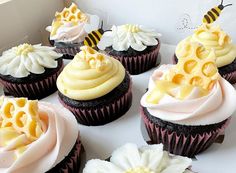 several cupcakes with frosting and decorations on them in a white cardboard box