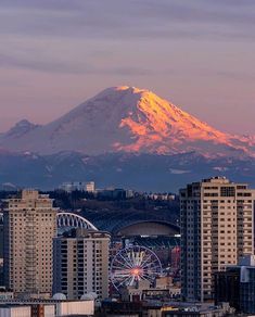 there is a mountain in the background with buildings around it and a ferris wheel on the foreground