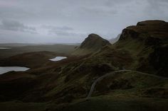 a winding road in the middle of a mountain range with water and grass on both sides