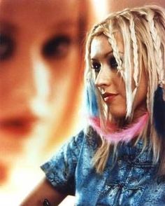 a woman with long blonde hair and dreadlocks standing in front of a movie poster