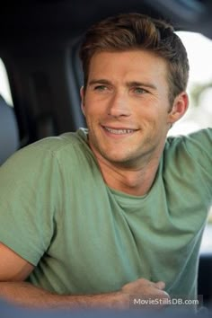 a man sitting in the back seat of a car with his hand on the steering wheel