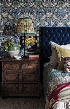 a bedroom with blue upholstered headboard and floral wallpaper on the walls