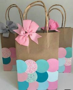 three paper bags with bows on them are sitting side by side, one is pink and the other is blue