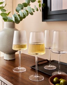 four wine glasses sitting on top of a wooden table next to a vase with green olives