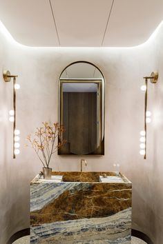 an elegant bathroom with marble counter tops and gold fixtures, along with lights on the wall