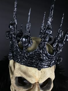 a skull wearing a black crown with skulls on it's head and two hands