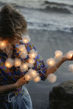 a young boy holding a cell phone while standing next to the ocean with lights on it