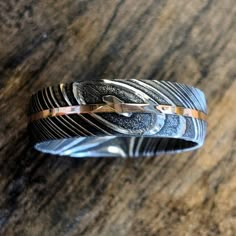 a wedding band that has been made with silver and gold inlays, on top of a wooden table