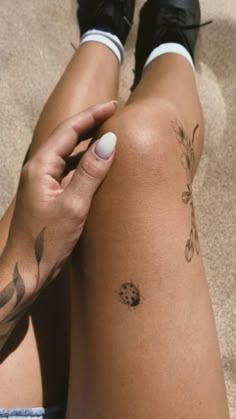 a woman's legs with tattoos on them sitting in the sand and holding onto her leg