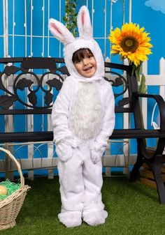 a little boy dressed in a bunny costume standing next to a bench with sunflowers