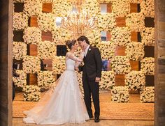 a bride and groom standing in front of a floral wall at their wedding reception with chandelier