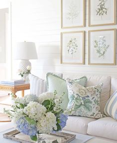 a living room filled with lots of white furniture and flowers on top of a coffee table